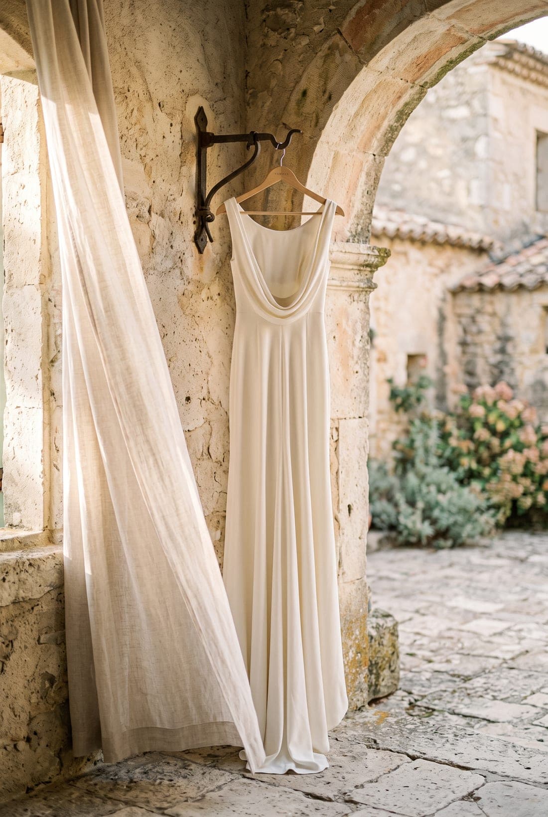 A silk wedding gown hanging in a sunlit stone archway