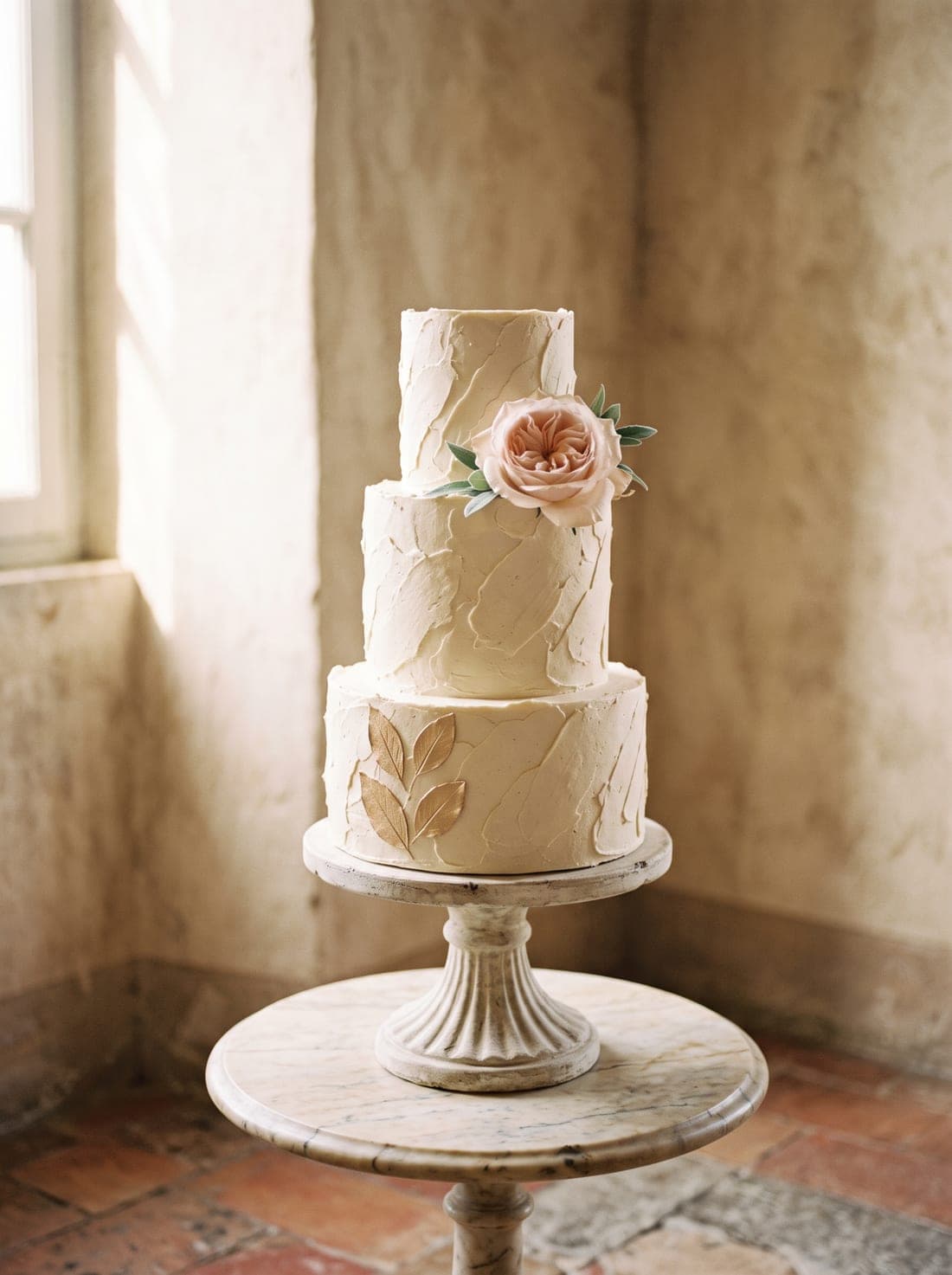 A three-tier buttercream wedding cake topped with a single blush rose